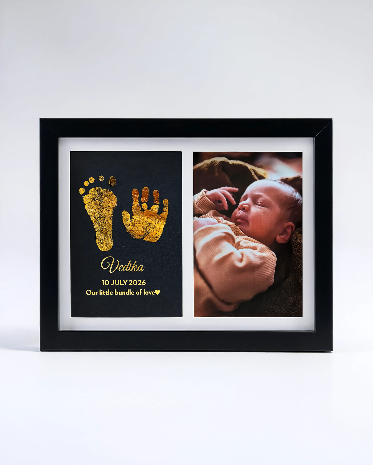 A black double-photo frame on a white background. The left photo slot shows gold baby foot and hand prints on a black background with the name 'Vedica' and date '10 JULY 2021'.