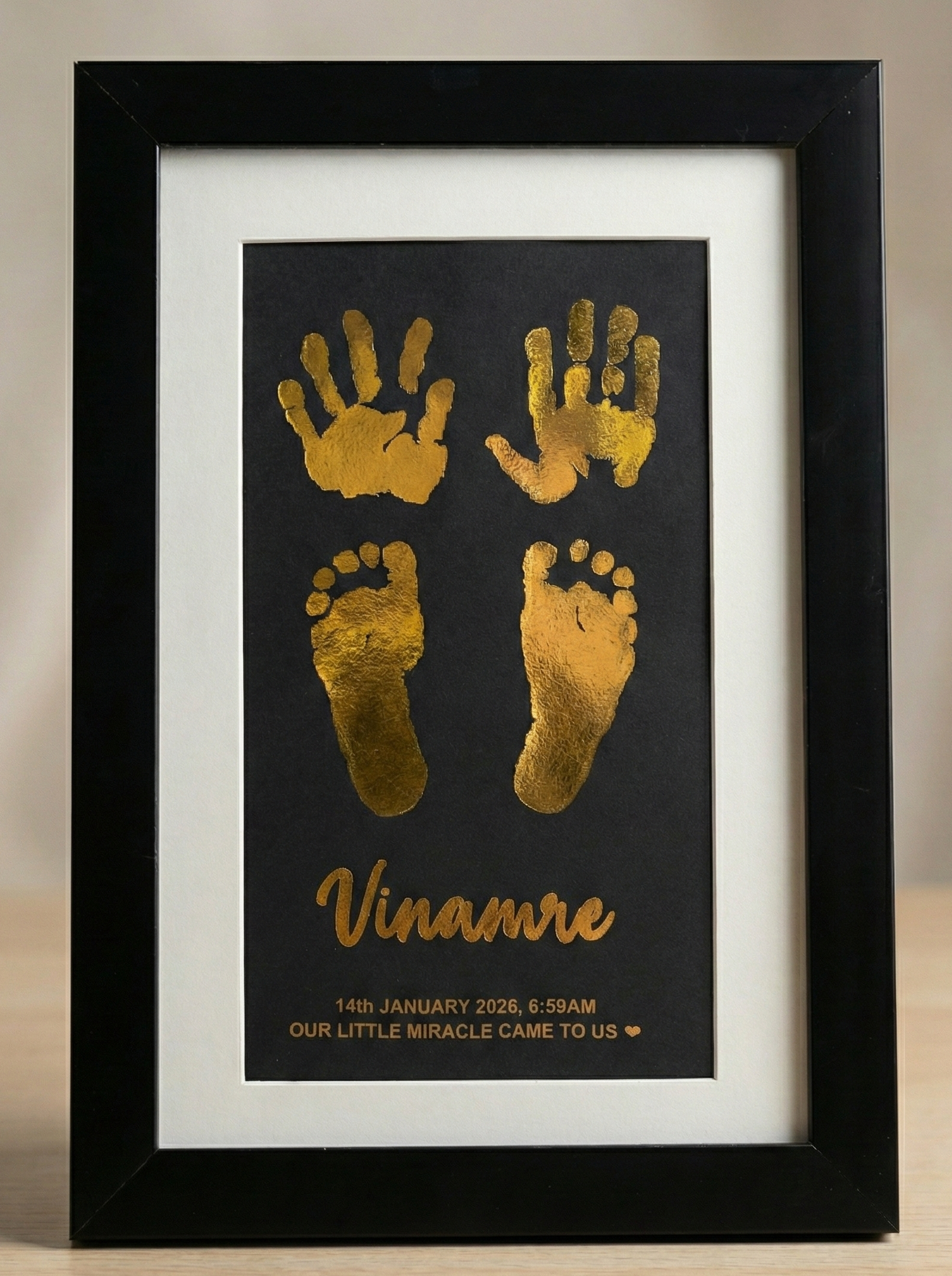 Framed artwork with gold hand and footprints and the name on a black background.
