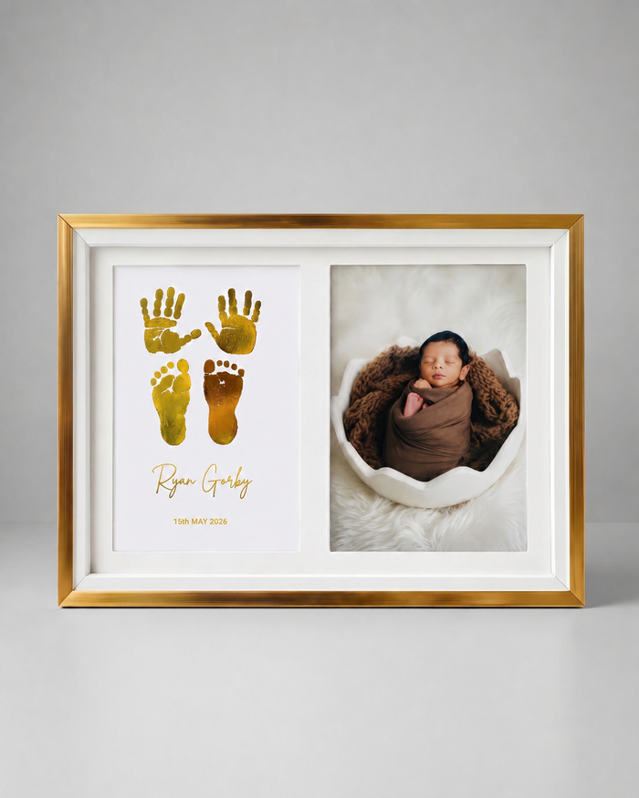A gold and white double-sided framed baby keepsake photo frame. The left side features a white background with gold foil baby handprints and footprints and the personalized name 'Ryan Grady' in gold script.