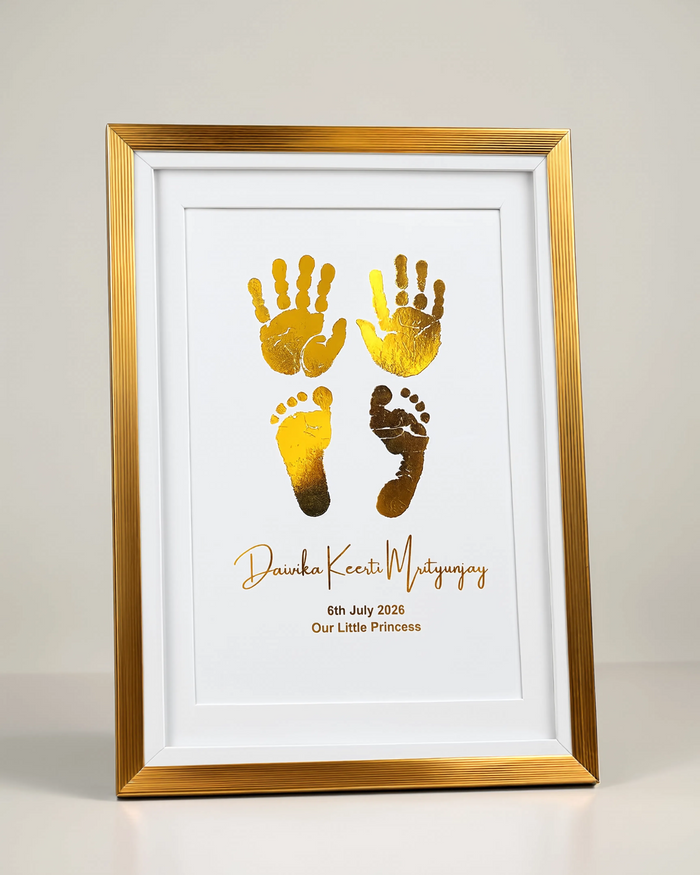 A framed personalized baby footprint and handprint keepsake print with metallic gold foil handprints and footprints on a white mat, set in a gold frame against a neutral light gray background.