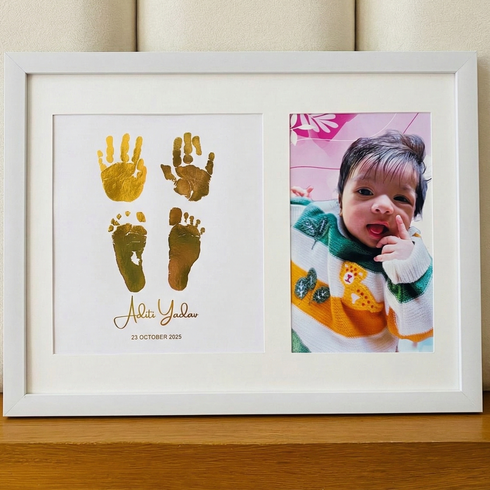 Framed artwork with gold handprints and footprints next to a photo of a baby on a wooden surface.