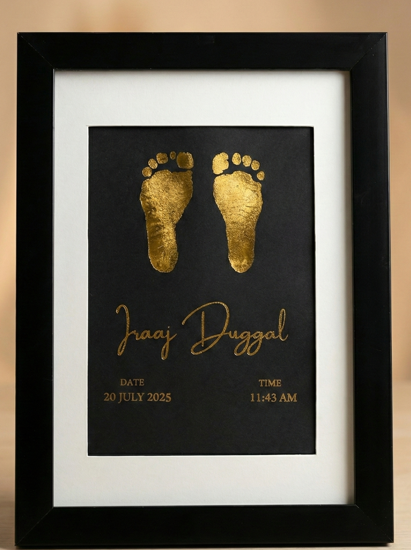 Framed artwork with gold baby footprints and name on a black background