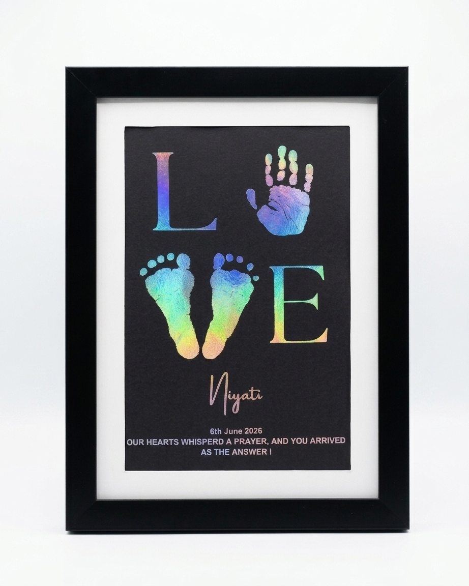 A framed personalized memorial print featuring the word LOVE with colorful baby footprints and handprints on a black background, enclosed in a black frame with a white mat.