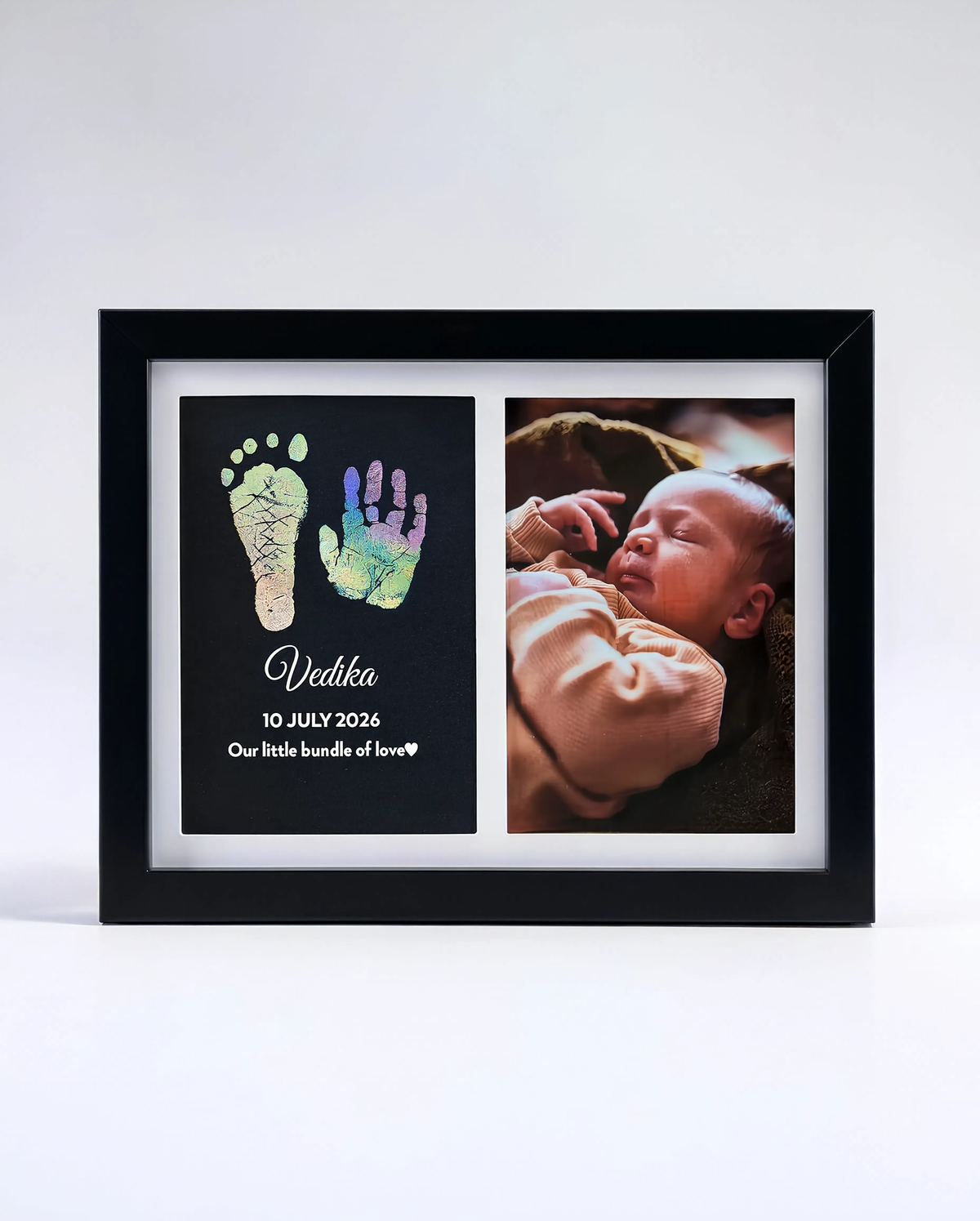 A black framed personalized baby keepsake photo print on a white background. The left panel shows colorful baby footprints and handprints with the name 'Vedika' and the date '10 July 2026'.
